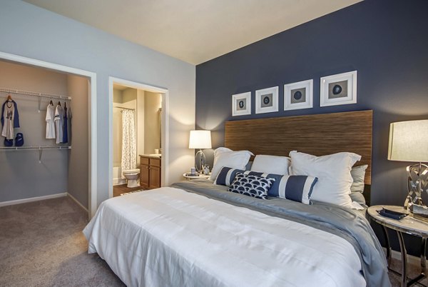 Elegant bedroom with plush bedding and large windows at Garrett West Apartments, showcasing modern luxury in a serene setting