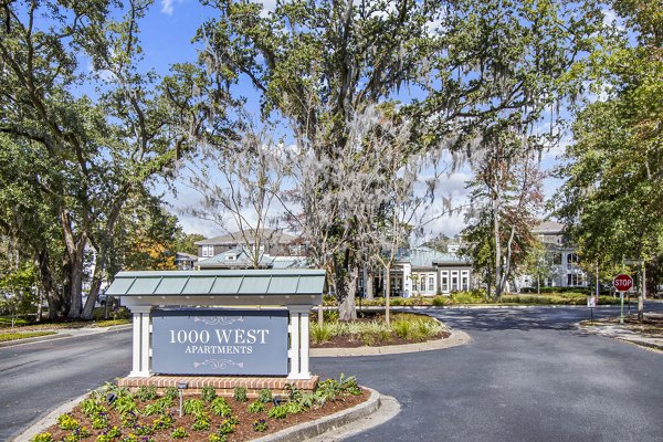 Entrance to 1000 West Apartments featuring a welcoming sign and lush greenery