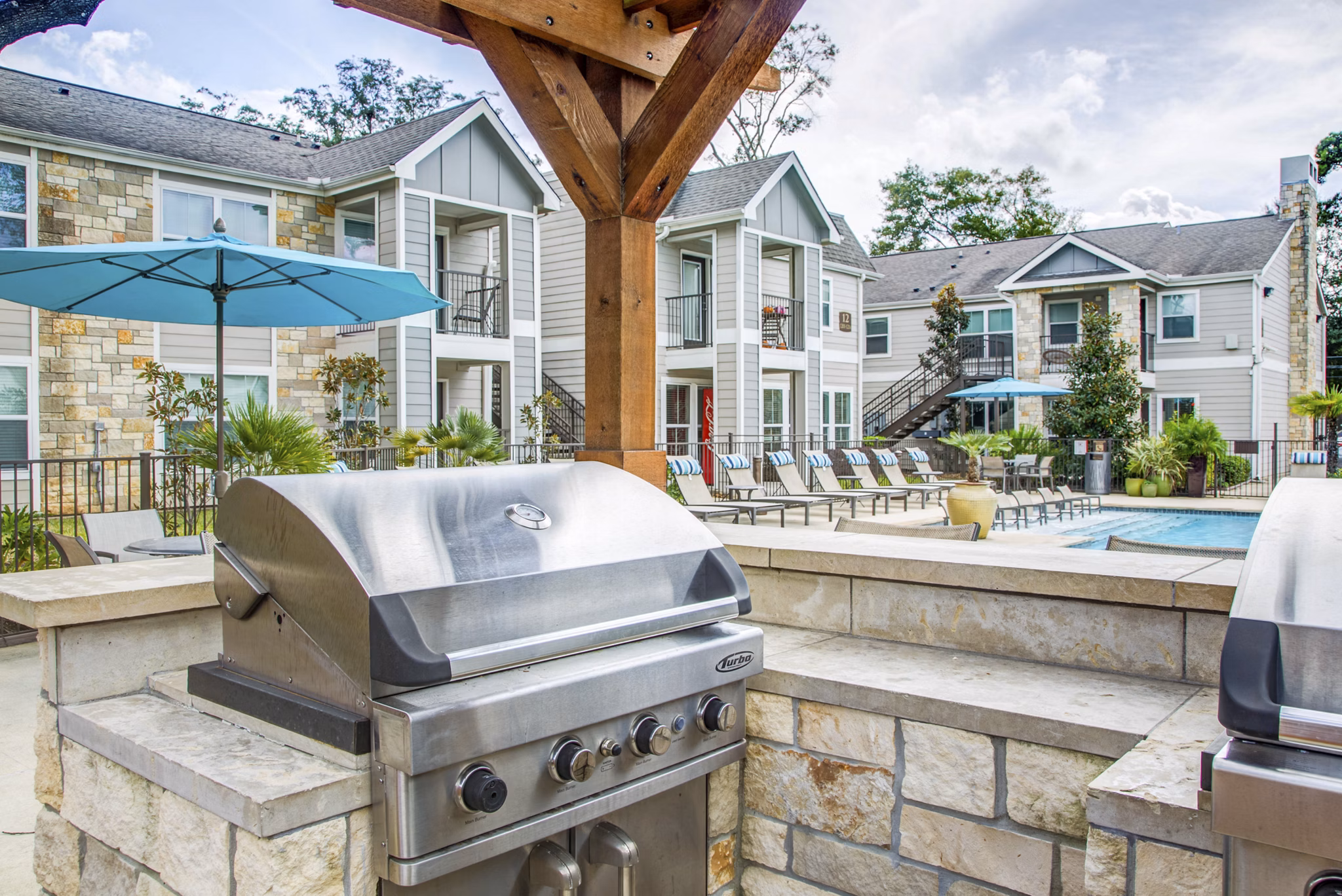 Outdoor grill area at Reserve at Garden Oaks Apartments with seating and lush greenery, perfect for gatherings in this luxury community