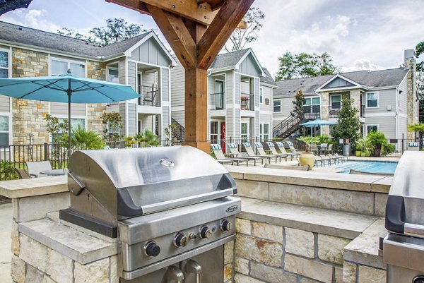 Outdoor grill area at Reserve at Garden Oaks Apartments with seating and lush greenery, perfect for gatherings in this luxury community