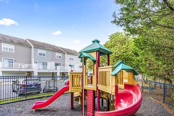 Children's playground area at Townes at Herndon Apartments featuring modern play structures and shaded seating spots