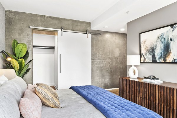 Cozy bedroom with modern decor at The Goodwin Apartments, featuring plush bedding and ample natural light for a luxurious living experience