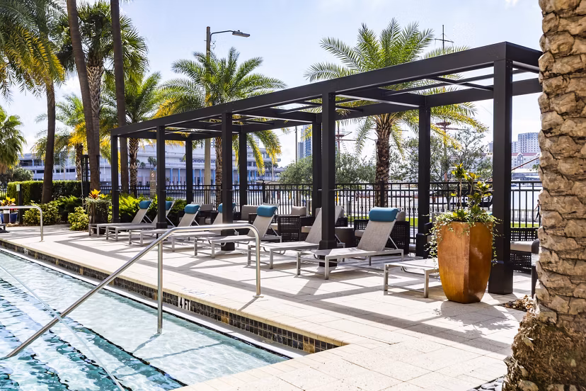 Relaxing outdoor pool area at 2 Bayshore Apartments featuring modern lounge chairs and lush landscaping