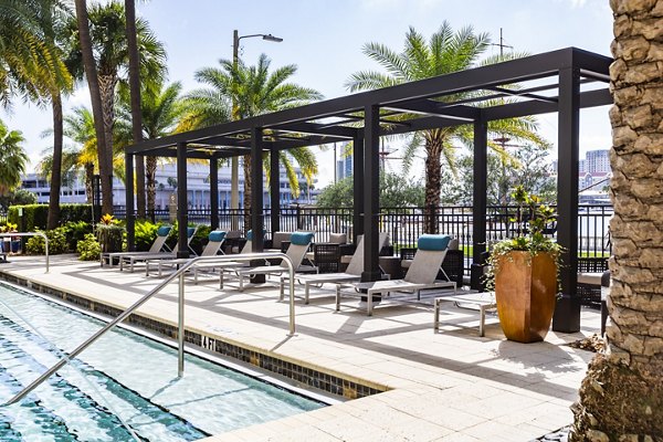 Relaxing outdoor pool area at 2 Bayshore Apartments featuring modern lounge chairs and lush landscaping