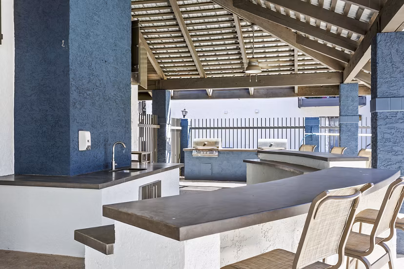 Outdoor grill area with seating at Fountain Palms Apartments, featuring lush landscaping for a luxury dining experience