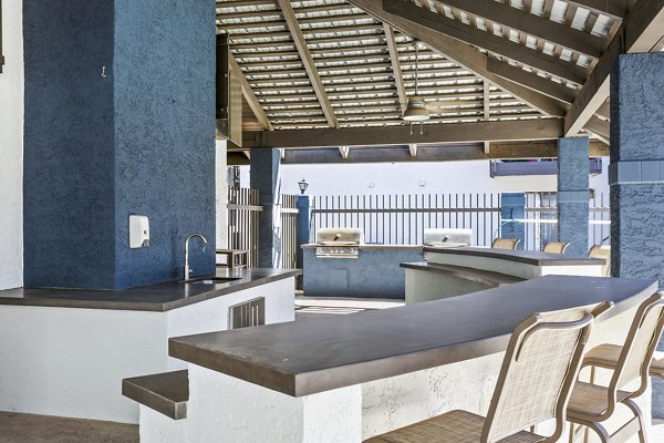 Outdoor grill area with seating at Fountain Palms Apartments, featuring lush landscaping for a luxury dining experience