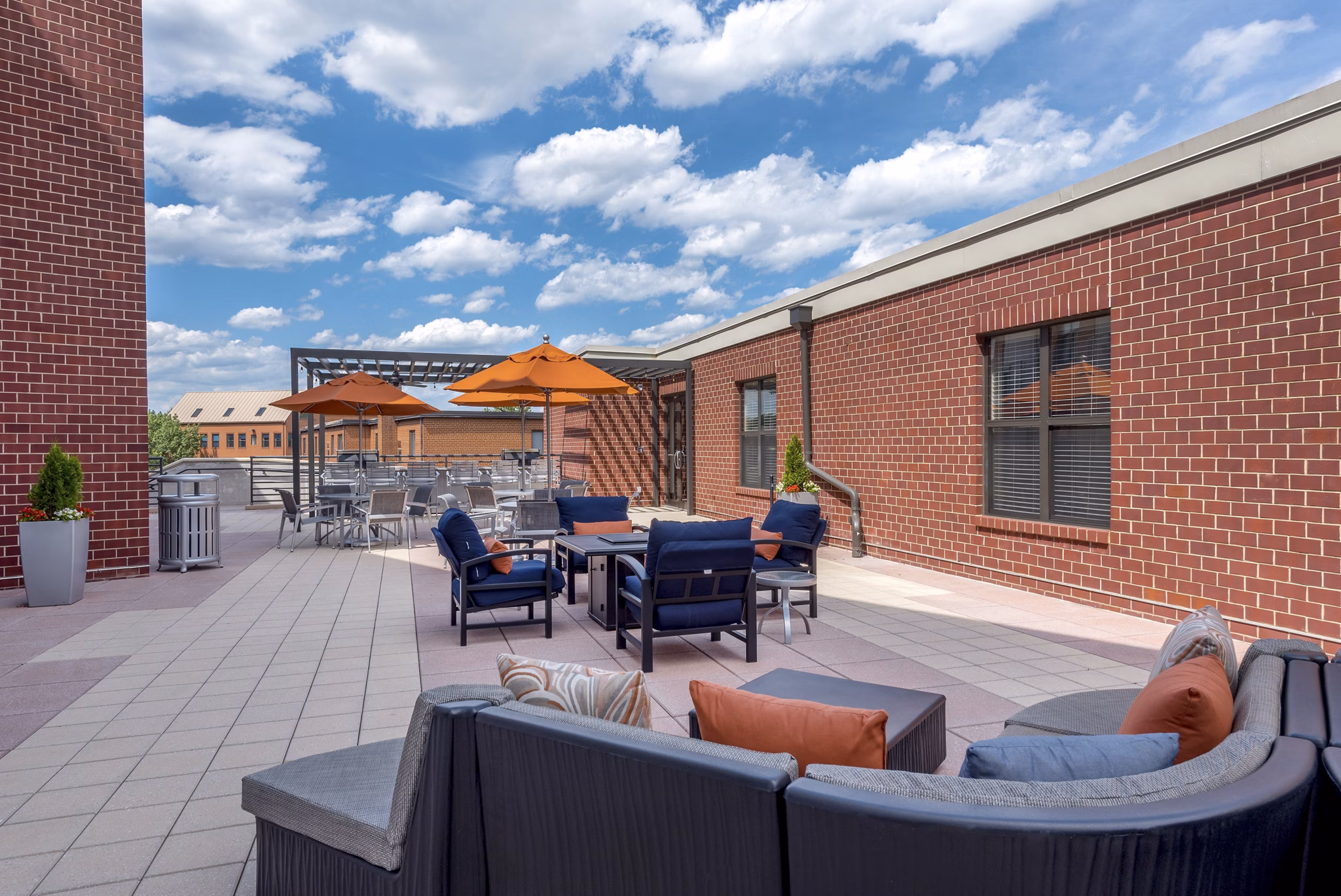Outdoor patio area with seating and umbrellas at luxury apartments with brick buildings in the background