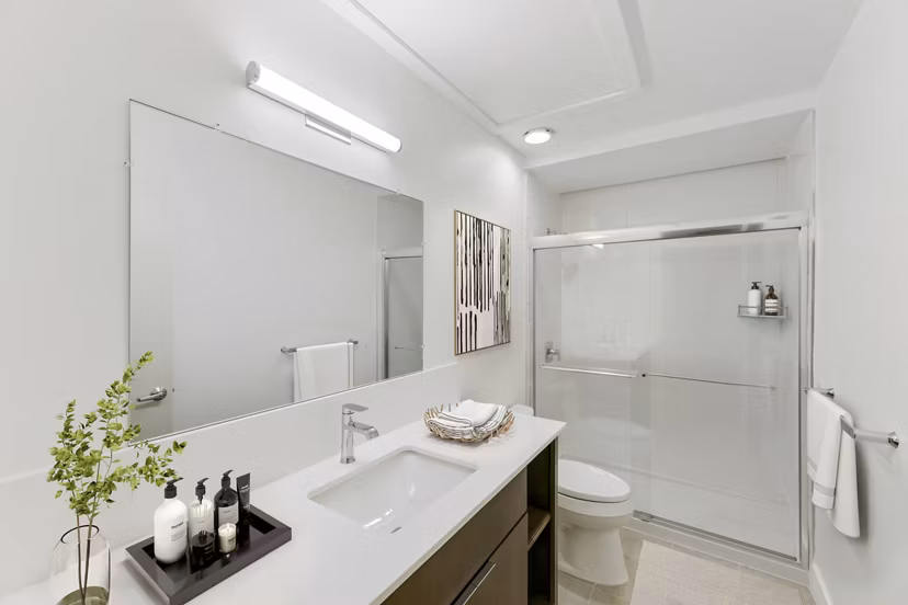 Bath with modern vanity and marble tiles at Louis at 14th Apartments