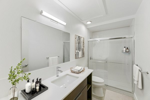 Bath with modern vanity and marble tiles at Louis at 14th Apartments