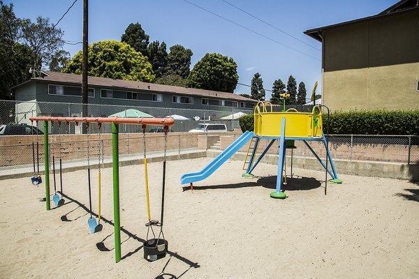Colorful children's playground at Ventura Terrace Apartments featuring swings and slides among landscaped greenery