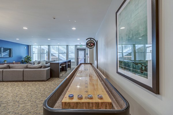 Game room with shuffleboard table and cozy seating area in luxury apartment