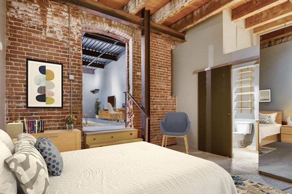 Cozy bedroom with exposed brick and large windows at Albers Mill Lofts Apartments