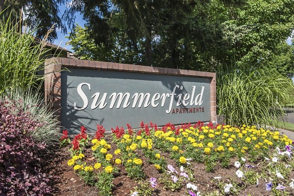 Summerfield Apartments sign surrounded by vibrant flowers and lush greenery in a welcoming outdoor setting