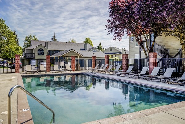 Resort-style pool area at Village at Cascade Park Apartments with lounge chairs and greenery