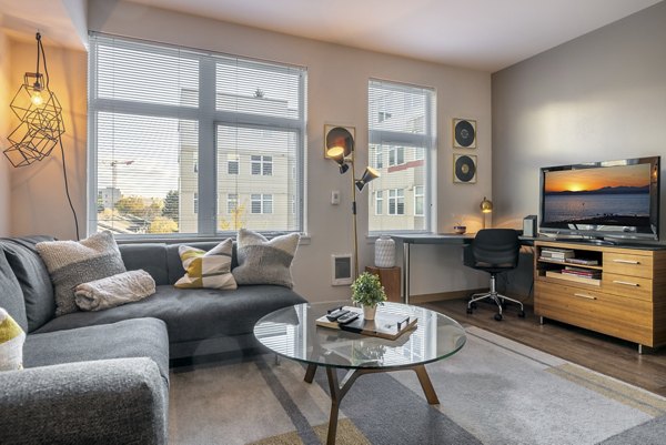 Modern living room with two brown leather sofas, a central coffee table, decorative pillows, and a view of a cityscape through large windows