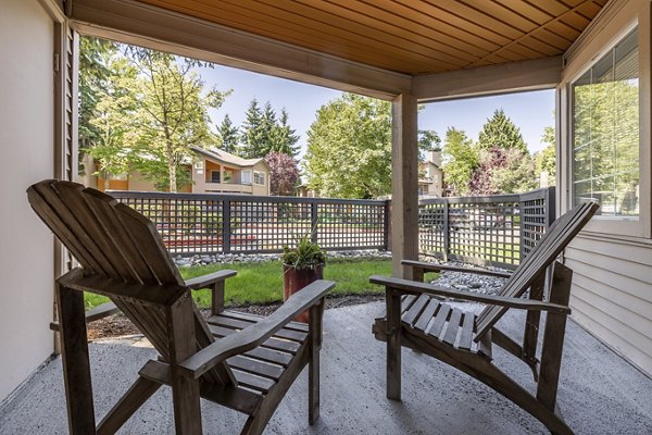 Cozy covered patio with two wooden chairs and a small table overlooking lush greenery and nearby buildings