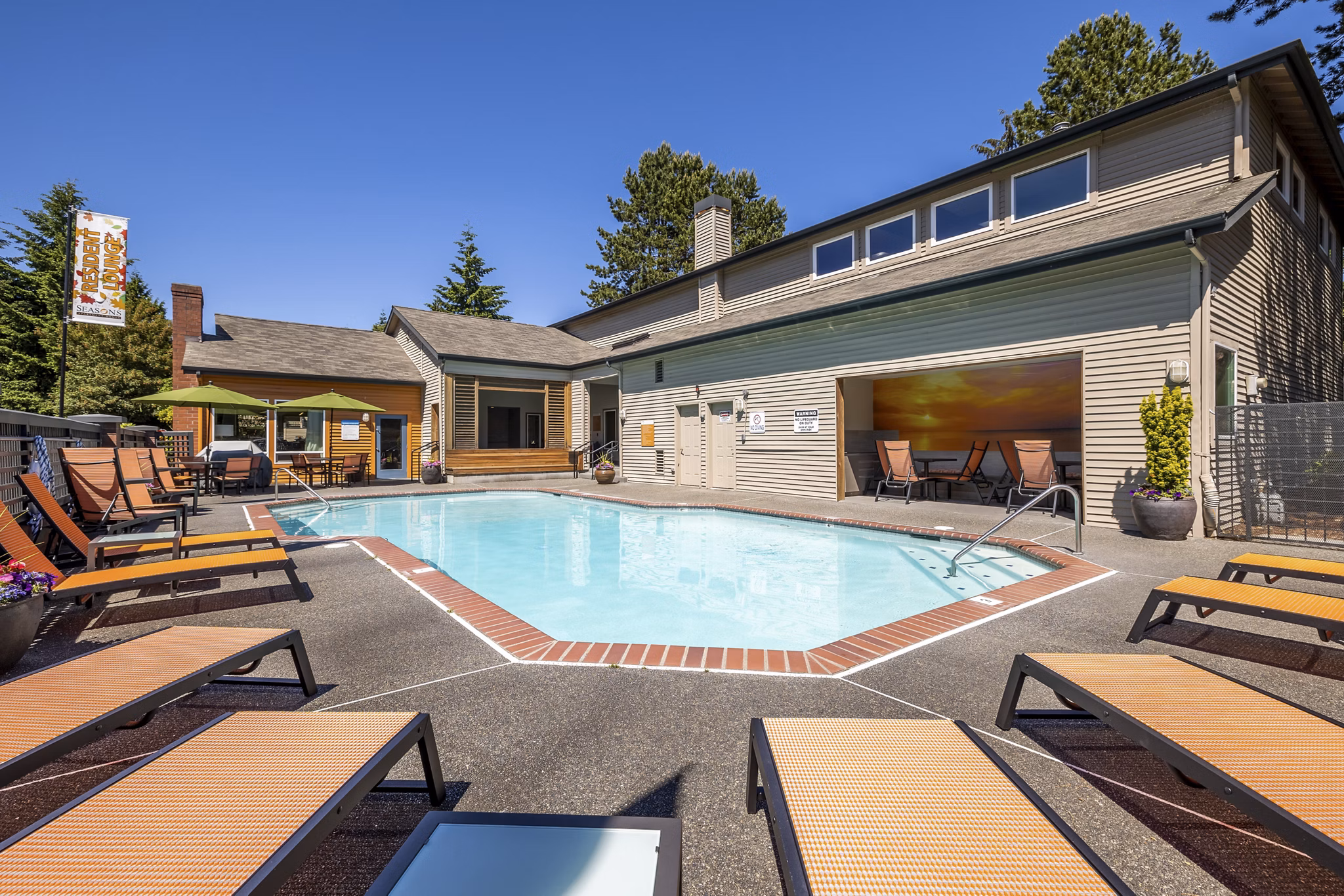 Sunlit pool area at The Seasons Apartments featuring lounge chairs and lush greenery, perfect for relaxation and recreation