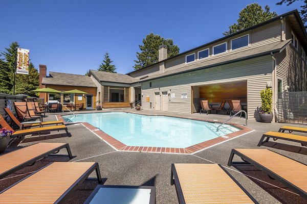 Sunlit pool area at The Seasons Apartments featuring lounge chairs and lush greenery, perfect for relaxation and recreation