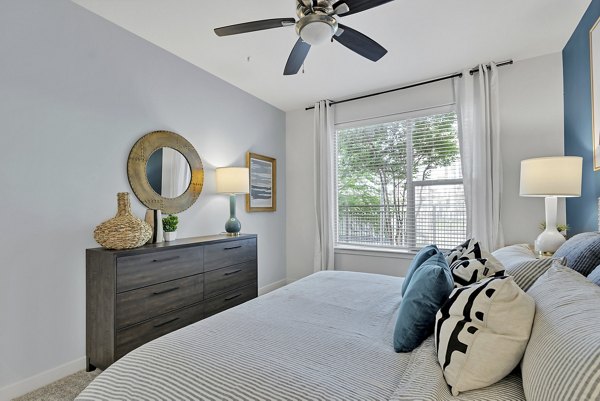 Comfortable bedroom with contemporary design and large window at Oak & Ellum Apartments