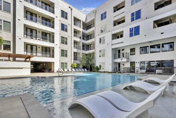 Luxurious outdoor pool at Oak & Ellum Apartments with modern lounge chairs and landscaped surroundings, perfect for relaxation and leisure