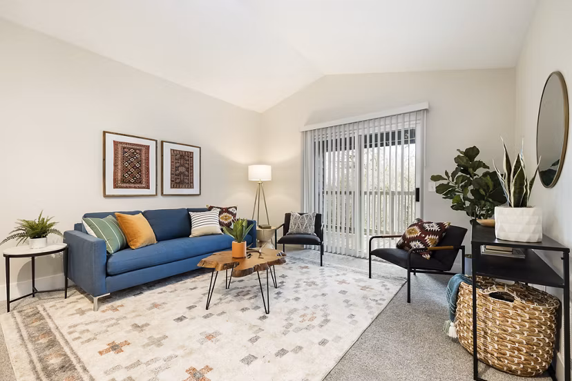 Modern living room featuring a blue sofa, decorative pillows, and sliding glass door with vertical blinds in luxury apartment