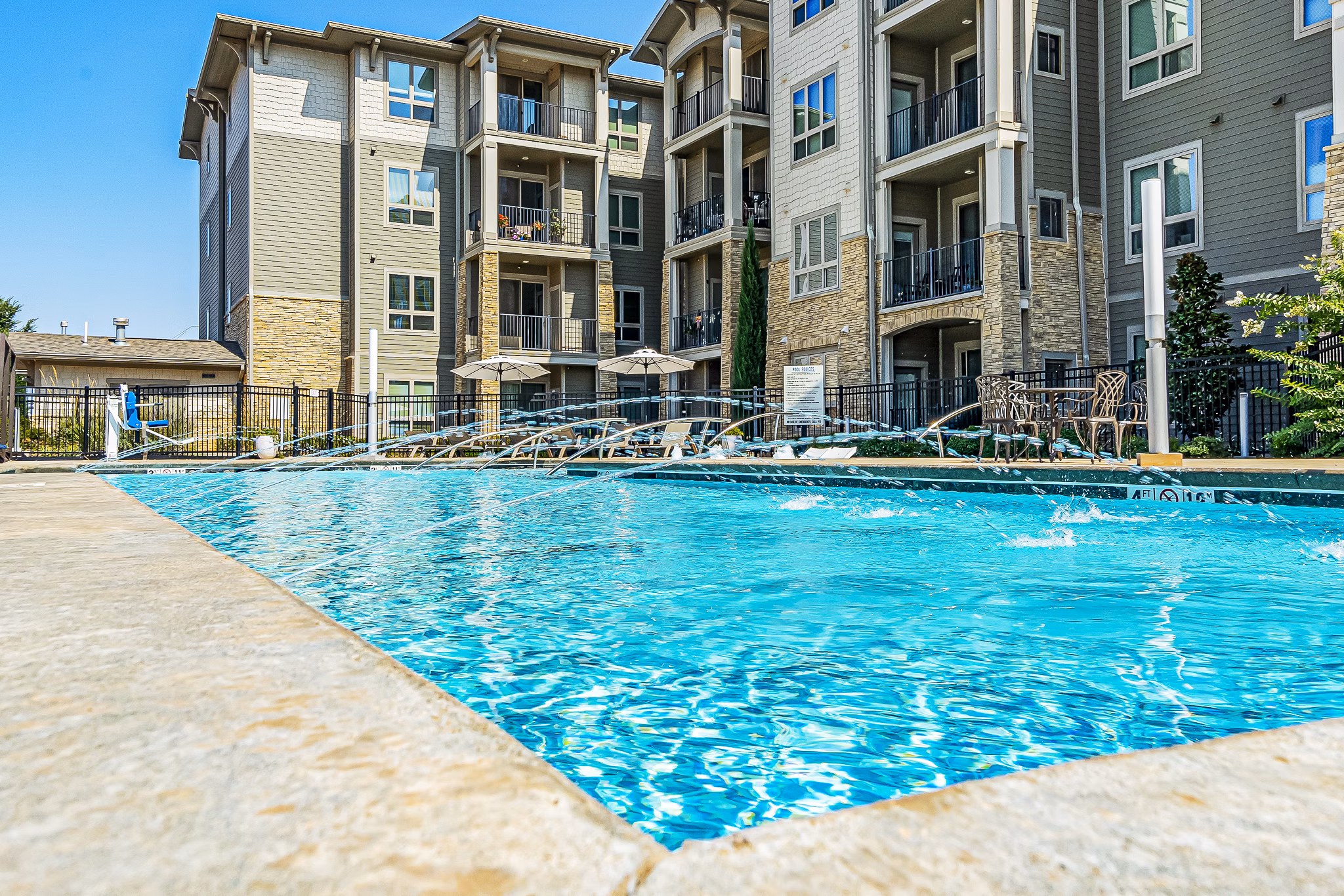 Modern outdoor pool area at Album Quail Springs Apartments with comfortable seating and lush landscaping