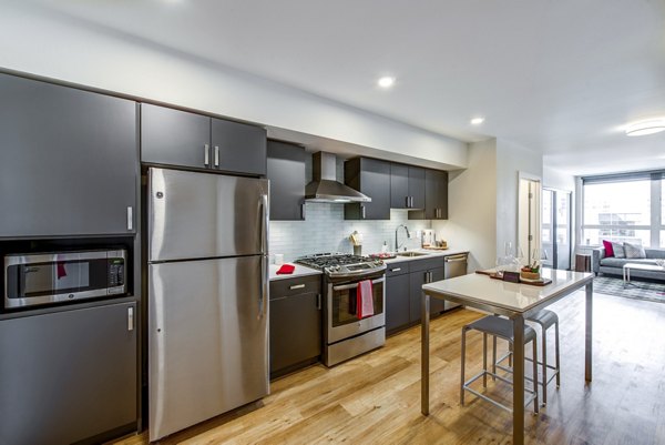 Open-concept kitchen with wooden flooring and modern appliances in Radius Apartments, featuring seamless living and dining spaces