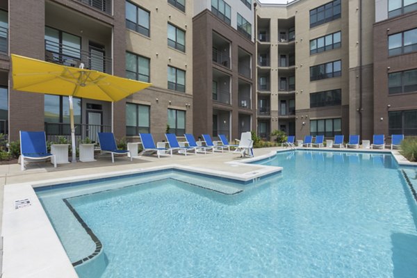 Sun-drenched outdoor pool area at 810 NINTH Apartments, a luxury Greystar property, featuring sleek lounge chairs and garden views