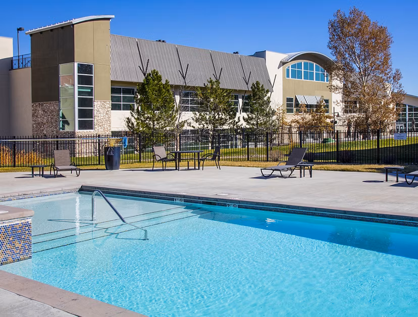 Swimming pool area with red Adirondack chairs next to a luxury apartment building