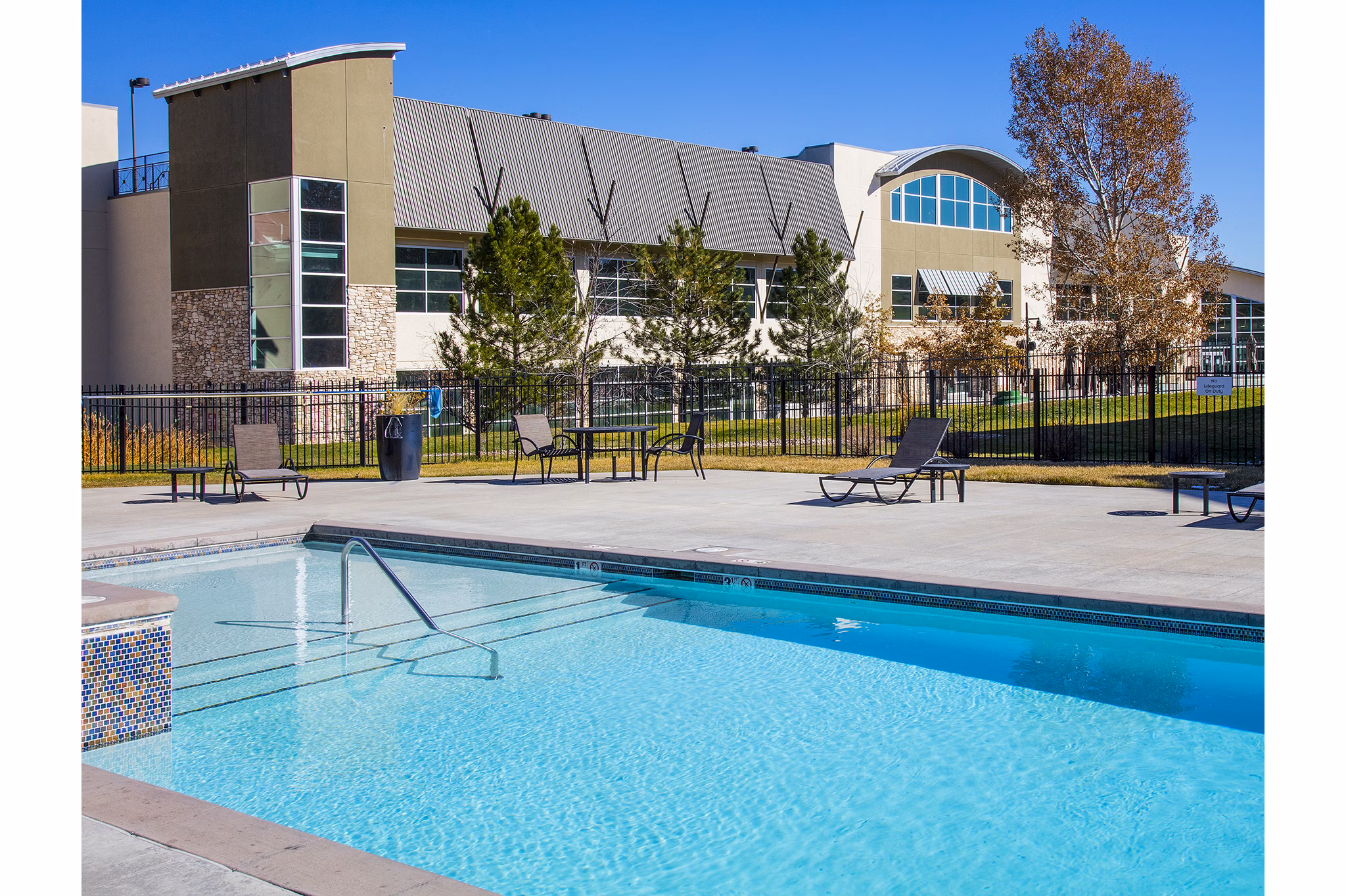 Swimming pool area with red Adirondack chairs next to a luxury apartment building