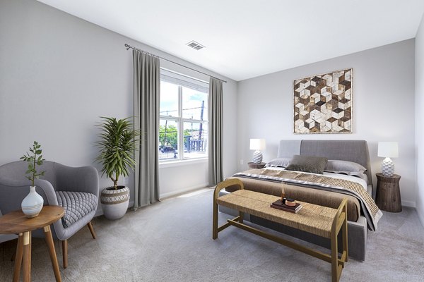 Cozy bedroom with modern decor at Rutherford Station Apartments, featuring a plush bed and stylish furnishings