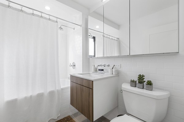 Sleek bathroom with white tiles, bathtub, and wooden vanity at The Chelsea Apartments