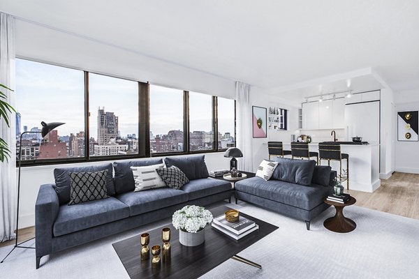 Spacious living room with city view, blue sofas, and kitchen at The Chelsea Apartments