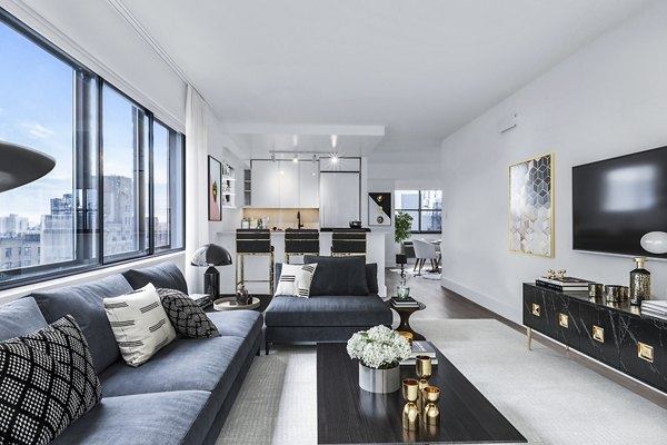 Sleek living room with large windows, black sofa, and decor at The Chelsea Apartments