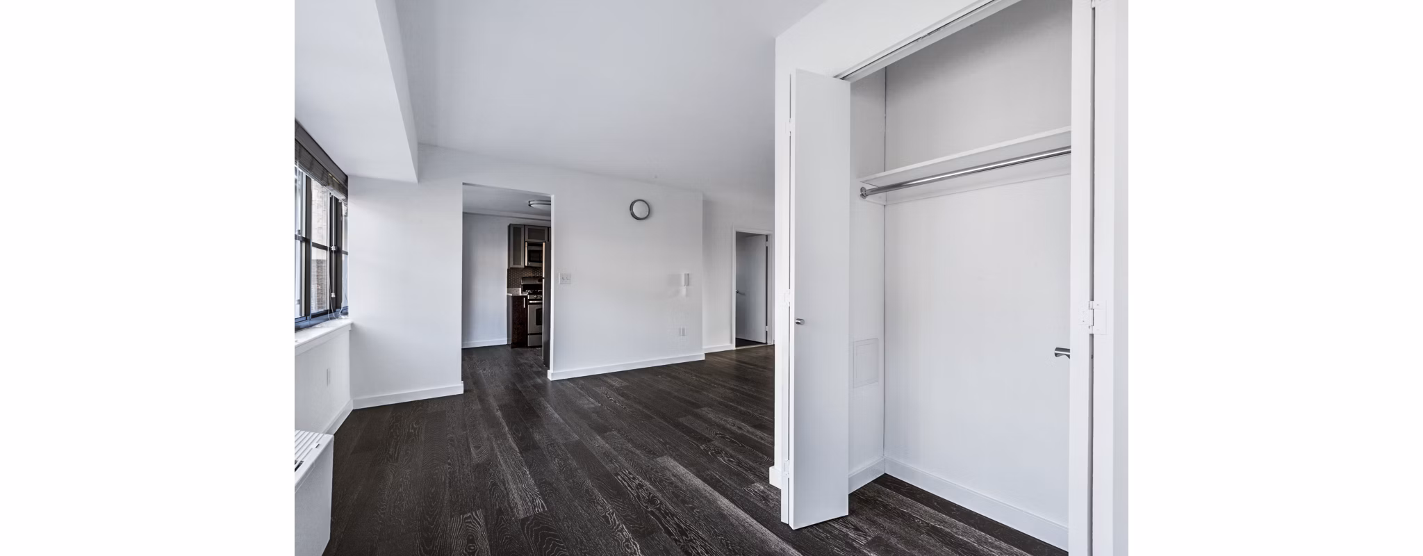 Empty room with open closet, dark wood floors, and white walls at The Chelsea Apartments
