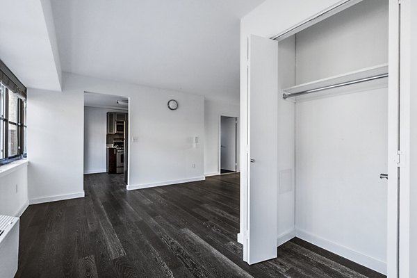 Empty room with open closet, dark wood floors, and white walls at The Chelsea Apartments