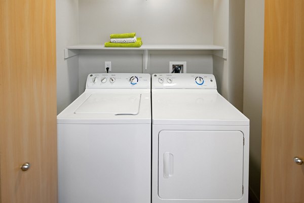 Laundry room featuring modern appliances at The Tennyson at Crescent Village Apartments