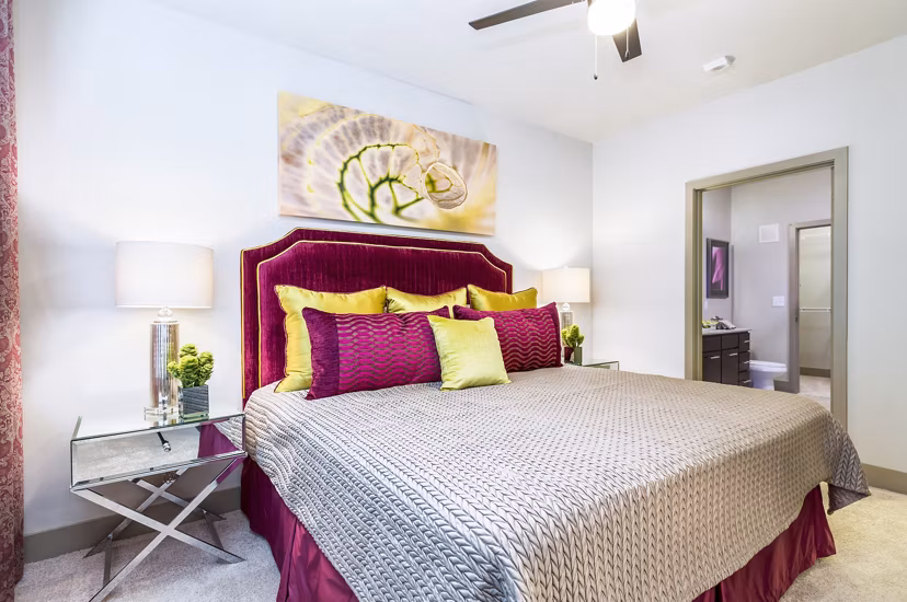 Bedroom with vibrant bedding, abstract wall art, and bedside lamps at Platform Apartments.