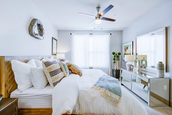 Bright bedroom with wooden bed, cozy pillows, and ceiling fan at Platform Apartments