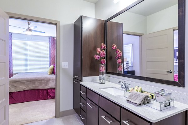 Elegant bathroom with dark wood cabinets, large mirror, and bedroom view at Platform Apartments