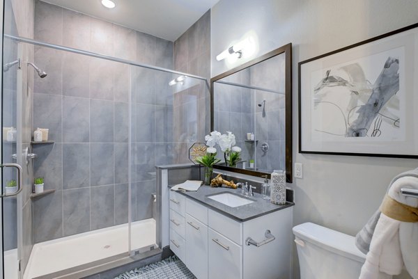 Sleek bathroom with glass shower, white vanity, and framed artwork in Platform Apartments