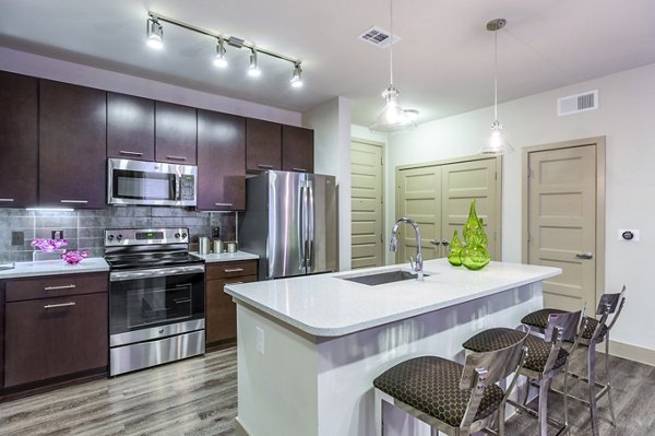 Elegant kitchen with stainless steel appliances and island with barstools in Platform Apartments