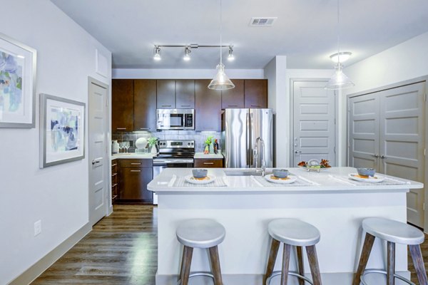 Spacious kitchen with island, bar stools, and stainless steel appliances at Platform Apartments