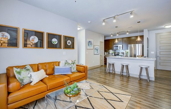 Open-concept living room and sleek kitchen with brown leather sofa at Platform Apartments, a luxury Greystar property