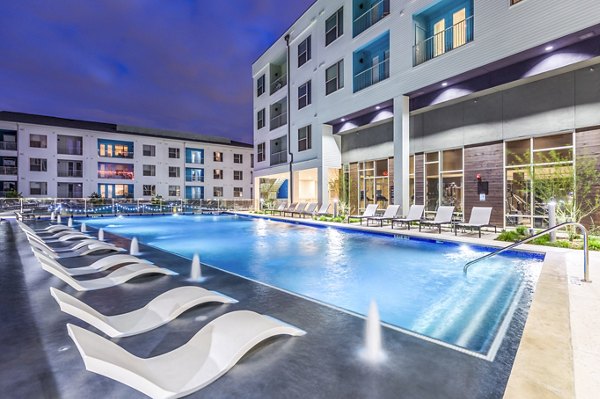 Apartment complex with illuminated pool and lounge chairs at night at Platform Apartments