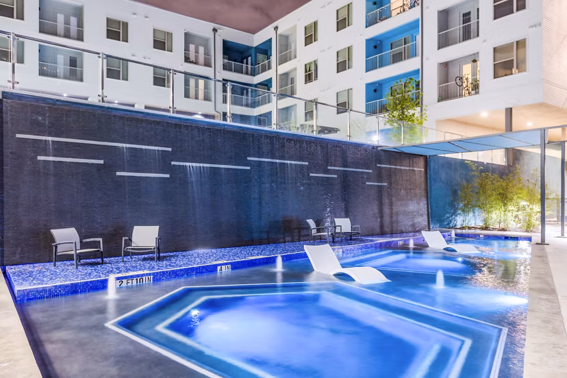 Illuminated pool area with lounge chairs and apartment building backdrop at Platform Apartments in downtown, a luxury community by Greystar