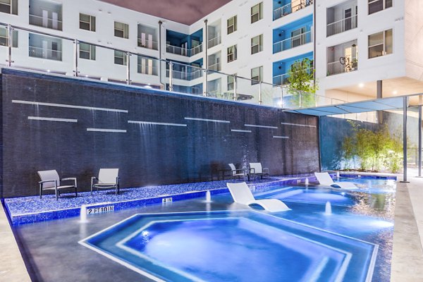 Illuminated pool area with lounge chairs and apartment building backdrop at Platform Apartments in downtown, a luxury community by Greystar