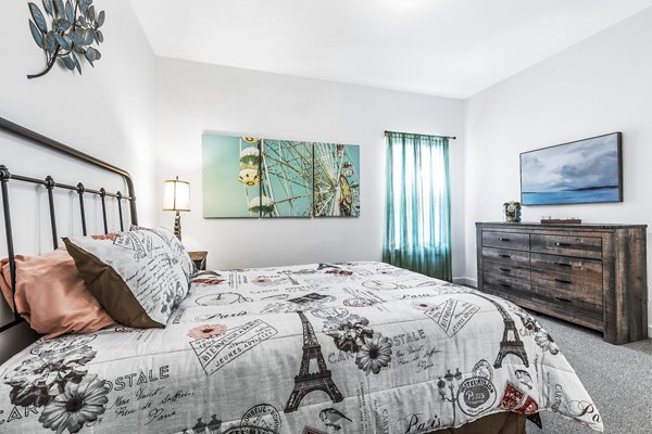 Cozy bedroom featuring modern decor and ample natural light at The Court at Dorel Apartments, a Greystar luxury community