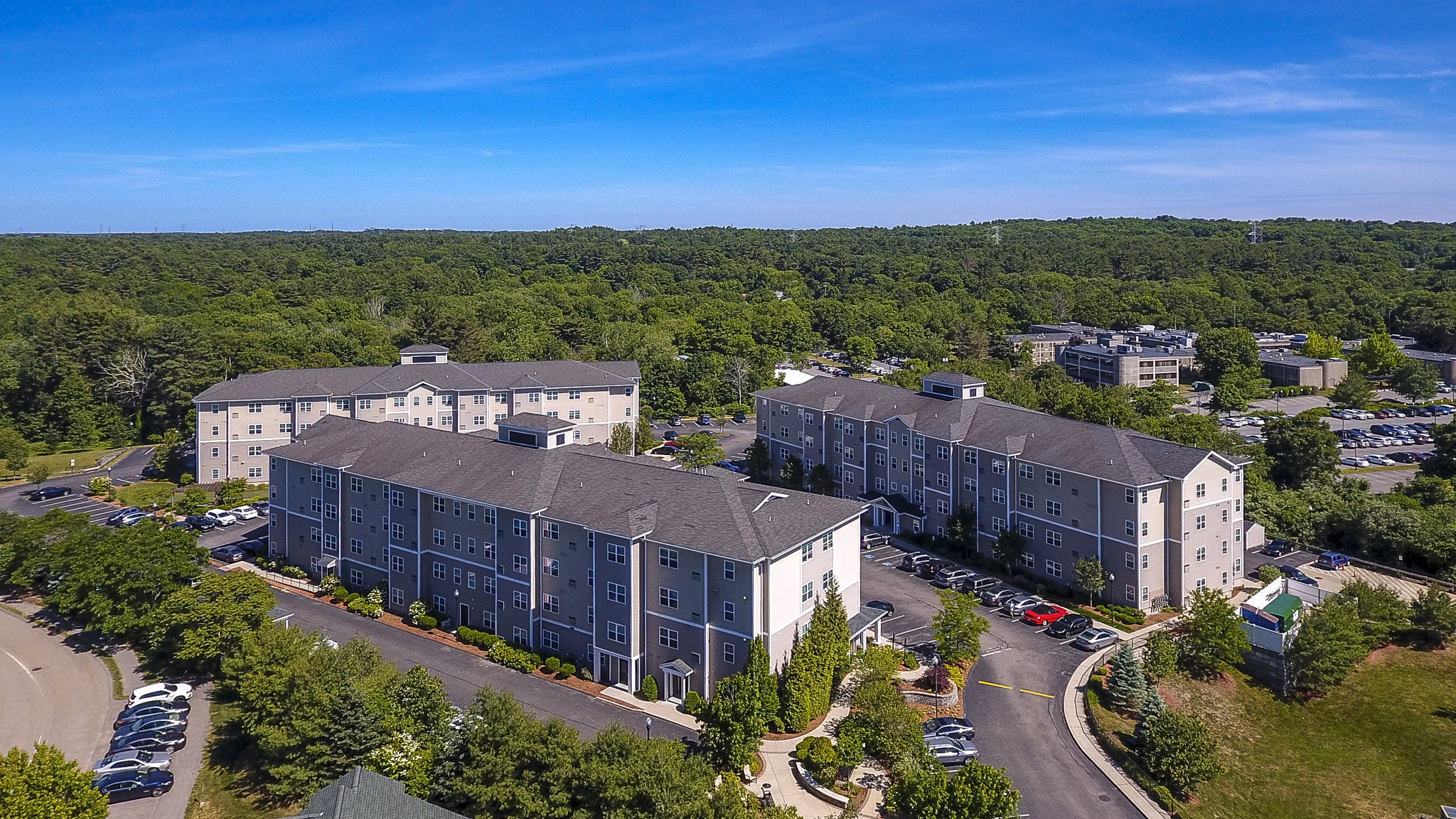 Aerial view of a luxury apartment complex with green trees and parking areas in a serene residential setting