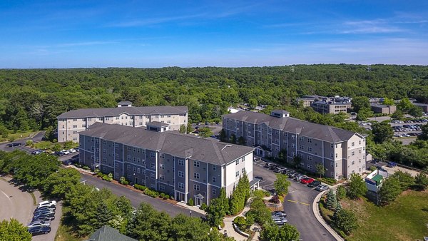 Aerial view of a luxury apartment complex with green trees and parking areas in a serene residential setting